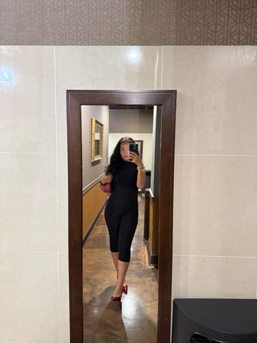 Customer's black Naked Sleeveless Capri Jumpsuit worn in a room, viewed in a mirror reflection.