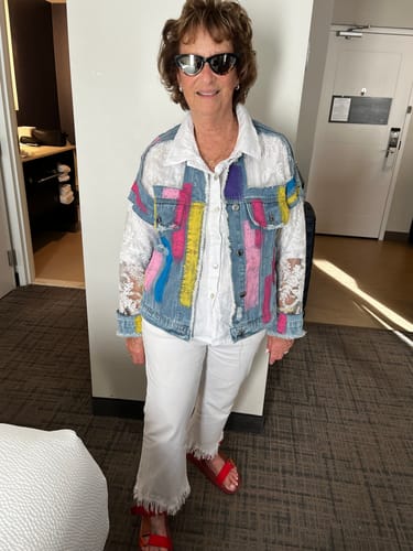 Reviewer wearing a colorful denim jacket with white lace sleeves over a white shirt and white pants.