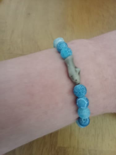Customer's wrist wearing a blue beaded Voyage Bracelet with a shark charm.