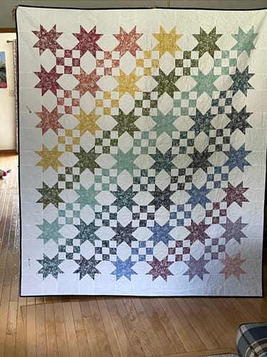 Customer's Star Studded quilt hanging on a wall, showing colorful star patterns on a white background