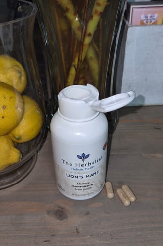 Customer's Lion's Mane capsules bottle with three open capsules on a wooden table near a glass bowl of lemons.