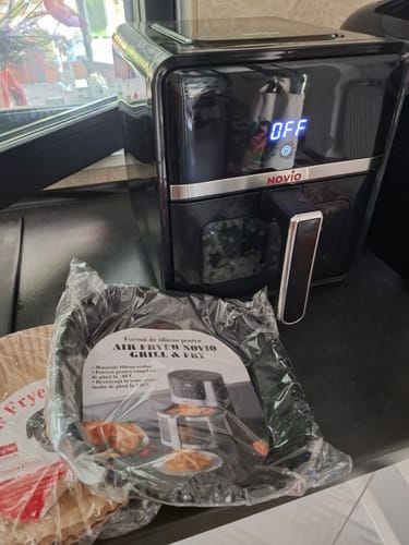 Customer's black Novio StonePro air fryer on a counter next to a new silicone air fryer liner in its packaging.