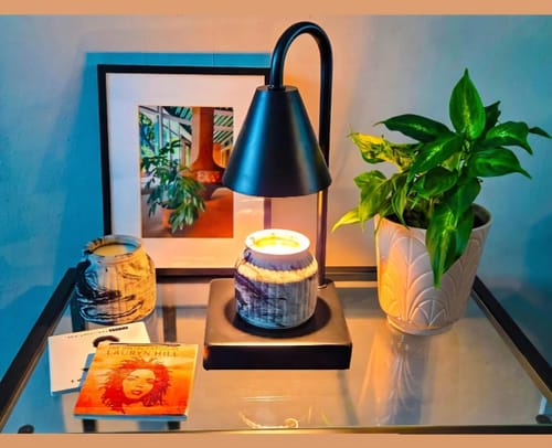 Customer's Deep Fall candle in a marbled jar warming under a black lamp on a glass table with a houseplant.