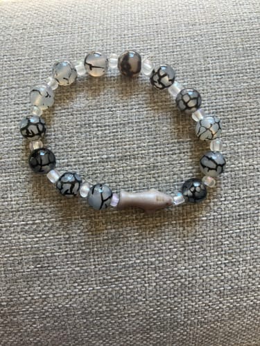 Customer's Voyage Bracelet showing a circular arrangement of patterned beads with a shark charm on a textured surface.