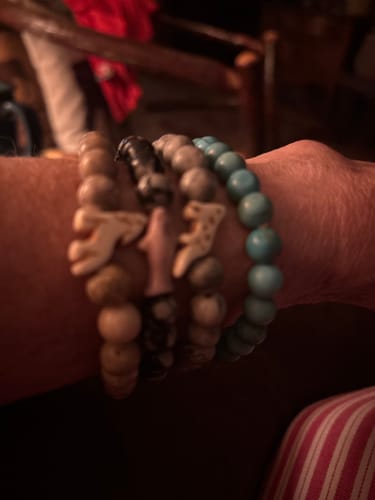 Customer's hand wearing four stacked Ascent Bracelets with decorative animal charms and bead textures.