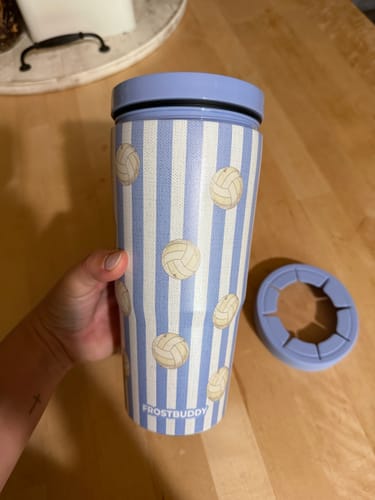 Reviewer holding a light blue, striped To-Go Buddy tumbler featuring a volleyball pattern.