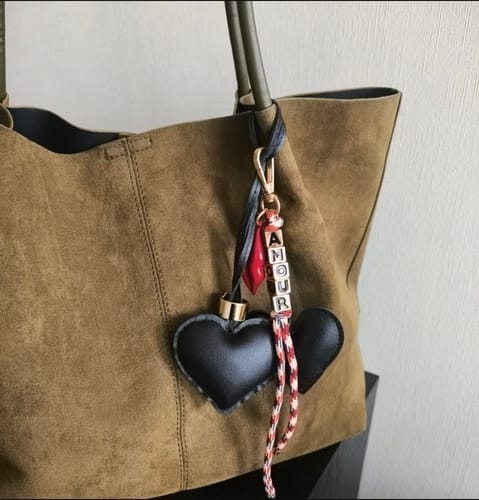 Reviewer's Llavero Amour keychain hanging on a green bag, featuring black hearts and beads with the word AMOUR.