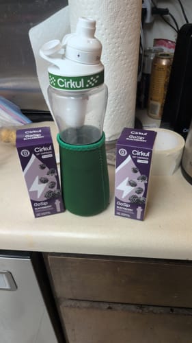 Customer's GoSip Blackberry water bottle in a green sleeve standing between two GoSip Blackberry flavor pod boxes.