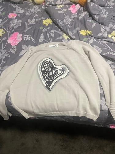 Customer's light-colored 707 FLAME KNIT SWEATER with heart-shaped design laid out on a patterned floral bedspread.