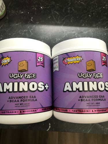 Customer's two UGLYFACE AMINOS+ tubs, one grape and one strawberry flavor, sitting on a dark counter.