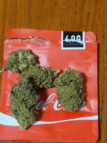 Customer's Cartel Cola THC-A flower buds on their bright red product packaging.