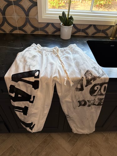 Customer's white Vale Forever Picasso Sweats featuring black paint-splatter designs and bold lettering on a counter.