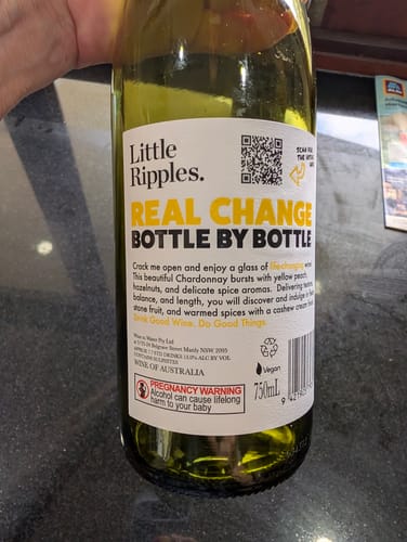 Customer's hold of a Little Ripples Chardonnay bottle showing the back label with text and impact information.