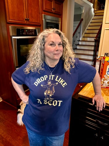 Customer's navy Drop It Like a Scot T-Shirt with graphic print on a person standing in a kitchen.