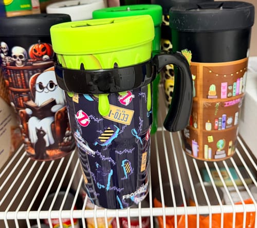 Customer's To-Go Buddy Ghostbusters Ecto Car cup with green lid and handle on a wire shelf with other decorated tumblers.