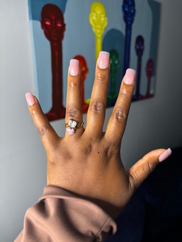 Customer's hand wearing the Navae Birthstone Ring with a pear-cut pink stone and a square-cut clear stone.