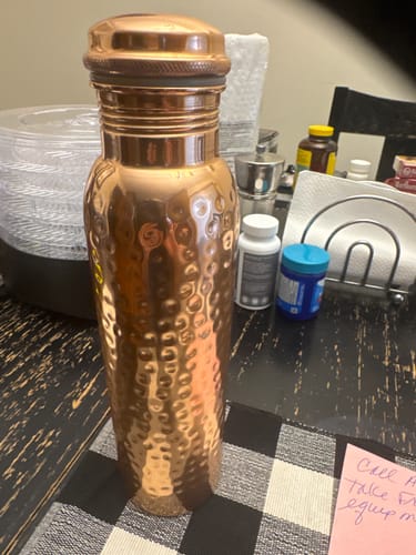 Customer's hand-hammered copper Ayurveda water bottle standing on a table among household items.