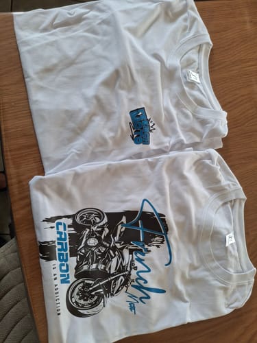 Customer's two white COLLECTION SP t-shirts featuring blue graphics of a motorcycle, laid flat on a wooden table.