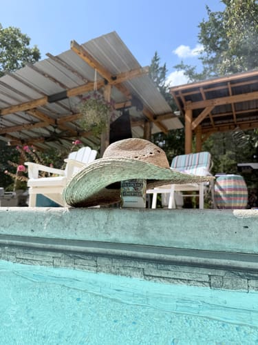 Customer's Margaritaville Universal Buddy can cooler sitting on a pool ledge, shaded by a straw hat.