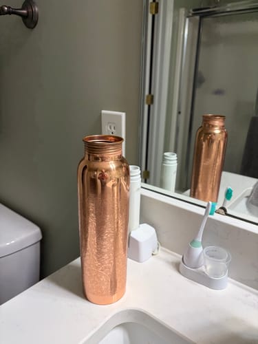 Reviewer's copper water bottle sitting on a bathroom vanity next to a toothbrush.