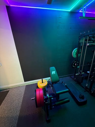 Reviewer's RitFit PLC01 Leg Extension Curl Machine set up in a home gym with colorful weight plates.
