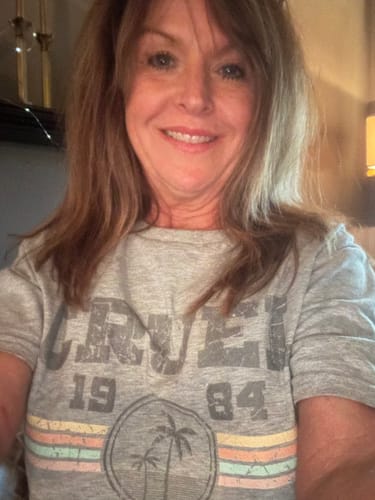 Reviewer wearing a grey Cruel Summer 1984 t-shirt with a palm tree graphic, looking at the camera.