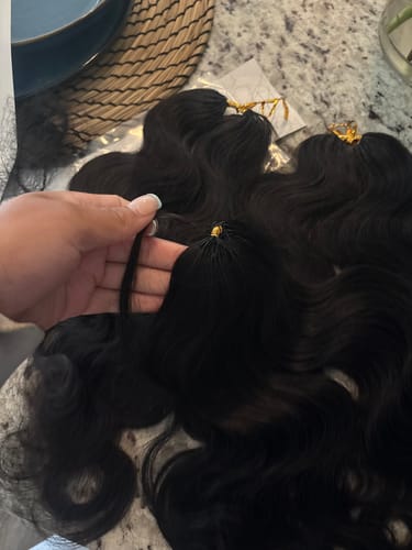 Customer's hand holding black Miracle Knots crochet hair bundles showing the body wave texture.