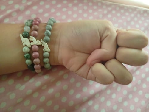 Reviewer's wrist wearing three Scout Bracelets with white wolf charms against a pink dotted background.