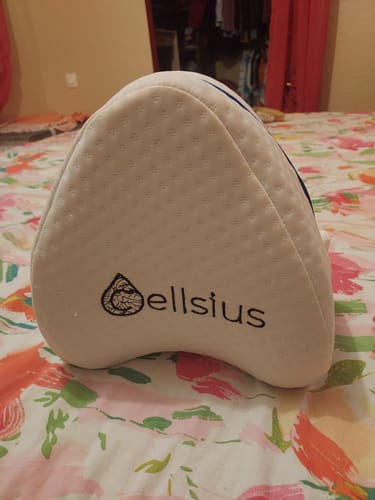 Customer's white Cellsius knee cushion with branded logo, resting on a colorful patterned bedspread.