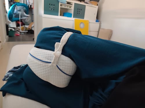 Reviewer's Cellsius coussin genoux avec une housse blanche et bleue, positionné entre des jambes sous une couverture.