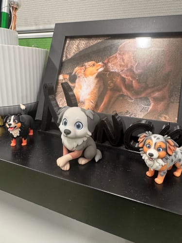 Customer's three custom-made dog figurines displayed on a shelf in front of a framed pet photo.