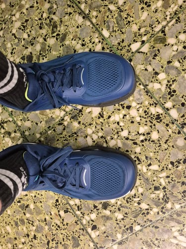 Customer's feet wearing blue CUURT Muuv wide toe box court shoes on a textured floor.