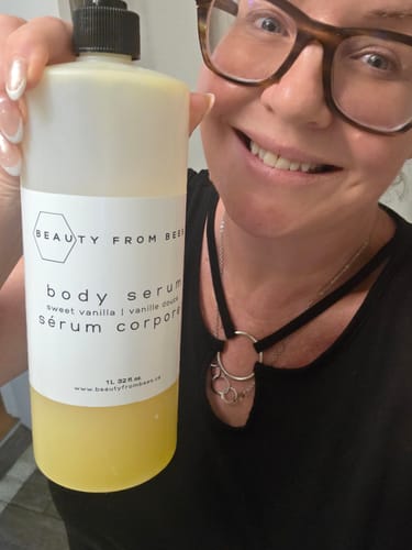 Customer's hand holding a bottle of Beauty From Bees Body Serum, smiling face partially visible.
