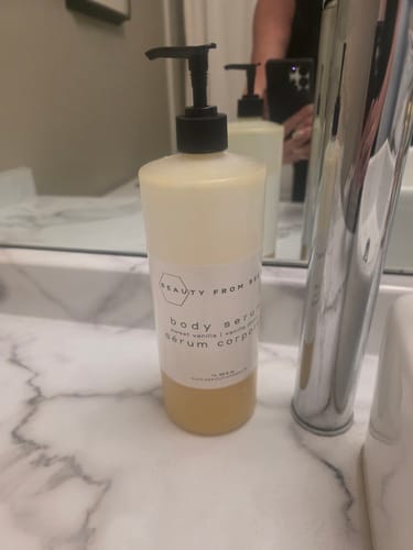 Customer's bottle of Beauty From Bees Body Serum sitting on a marble bathroom counter.