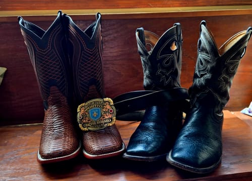 Customer's Cognac Python Leather Boots with square toe, standing next to a pair of black boots on a wooden bench.