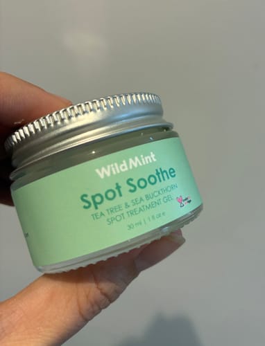 Customer's hand holding a small glass jar of Spot Soothe treatment gel with a green label.