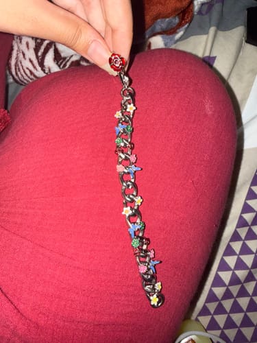 Reviewer holding a silver-toned link bracelet adorned with colorful floral charms against a red fabric background.
