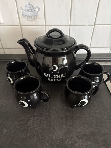 Customer's black Witches Brew teapot and four small mugs with moon and star designs on a dark counter.