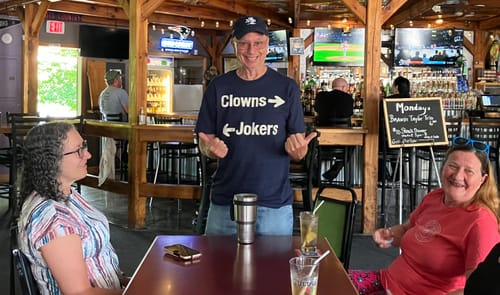 Customer's dark blue Clowns and Jokers Basic T-Shirt worn by a smiling person in a casual bar setting.