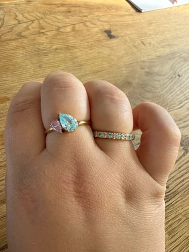 Reviewer's hand wearing the gold Eterna Birthstone Ring with pink and blue stones alongside another ring
