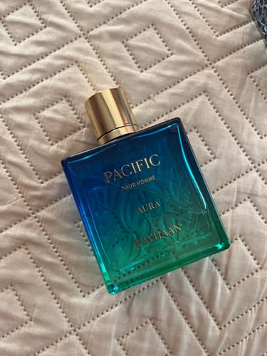 Customer's Rayhaan Pacific Pour Homme Aura perfume bottle with a blue to green gradient, resting on a textured fabric.