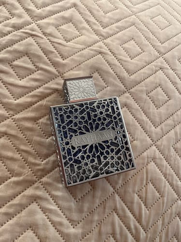 Customer's Rayhaan Aquatica perfume bottle with an ornate metallic lattice cap and frame, set on a textured beige quilt.