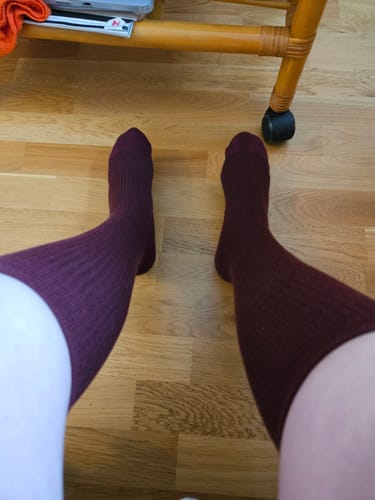 Customer's feet wearing dark red Diasocks stödstrumpor while sitting on a wooden floor.