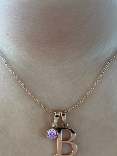Customer's Birthstone Initial Necklace, featuring a gold letter B pendant and a small, pink cubic zirconia stone.