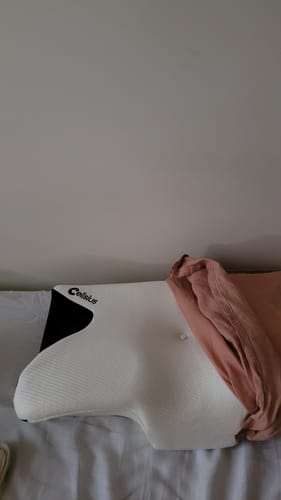 Customer's Oreiller Papillon Cervical Cellsius partially covered by a dusty pink pillowcase on a bed.
