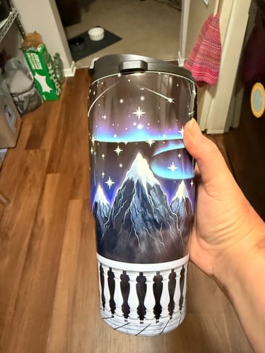 Customer's To-Go Buddy tumbler held in hand, showing a mountain landscape print with glowing stars and aurora.
