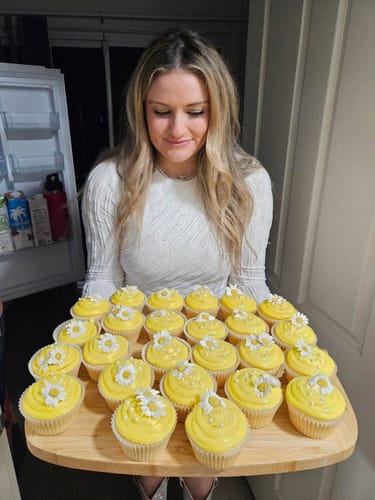 Customer's tray of bright yellow cupcakes topped with white daisies, held by a person in a white top.