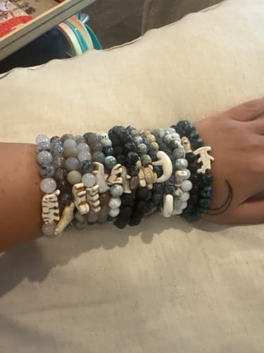 Customer's wrist wearing a stack of many multicolored Shark Week bracelets with various animal charms.