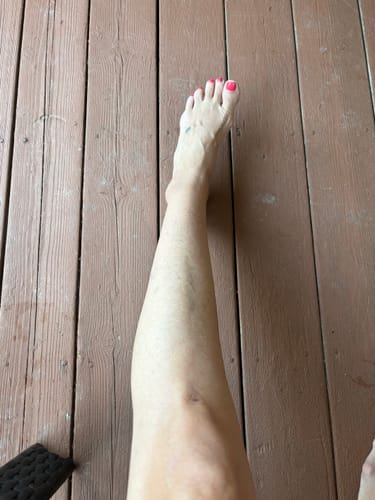 Customer's leg showing the subtle shimmering glow from the Body Serum - Summer Glow on wooden decking.