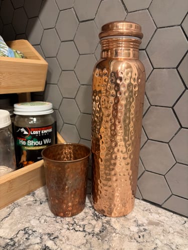 Customer's hand-hammered copper water bottle and matching tumbler sitting on a counter next to herbal supplements.